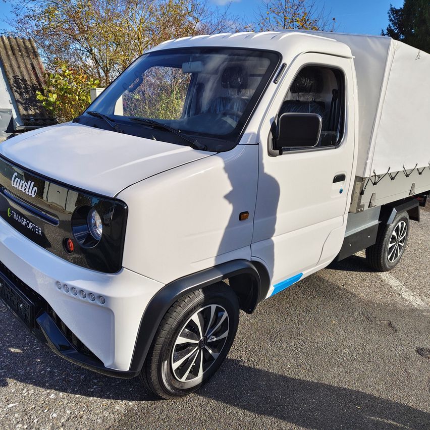 Ein weißer Lieferwagen namens 'Cacello' ist in einem Außenbereich mit Bäumen und einem Dach im Hintergrund geparkt.