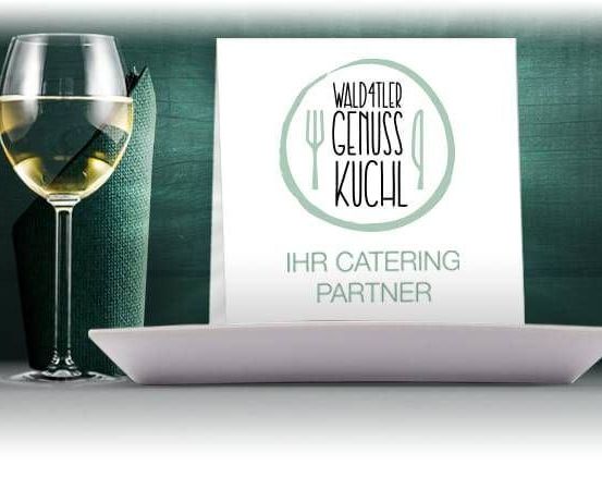 Ein Bild von einem Weinglas, einer gefalteten Serviette und einem Teller mit einer weissen Karte, die 'Waldfähler Genuss Kuchl Ihr Catering Partner' steht.