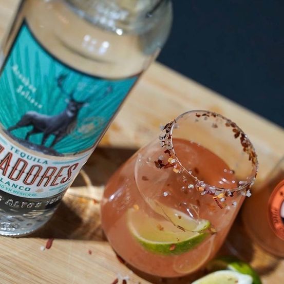 Eine Flasche Cazadores Tequila und ein Cocktailglas mit einem Getränk und Limettenscheiben auf einem Holztisch.