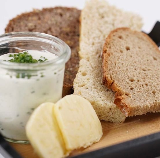 Ein Tablett mit verschiedenen Lebensmitteln, darunter ein Glas mit weißer Sauce, einem Stück dunklem Brot und zwei Scheiben Vollkornbrot.