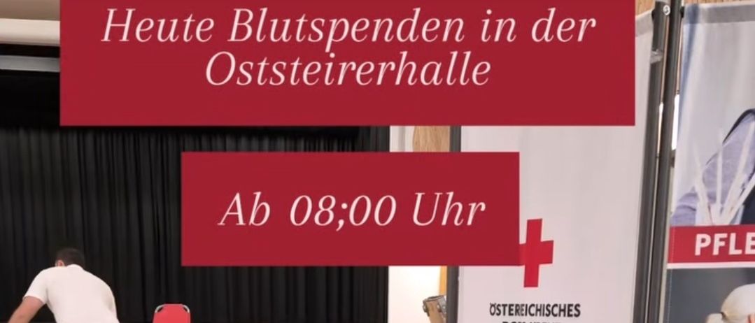 Eine Person in roter und weißer Uniform steht mit einer Kiste in einem Raum. Ein Banner mit der Aufschrift 'Blut spenden rettet Leben' und 'Österreichisches Rotes Kreuz' darunter. Ein weiteres Banner zeigt 'Oststeiernehalle Ab 08:00 Uhr'.