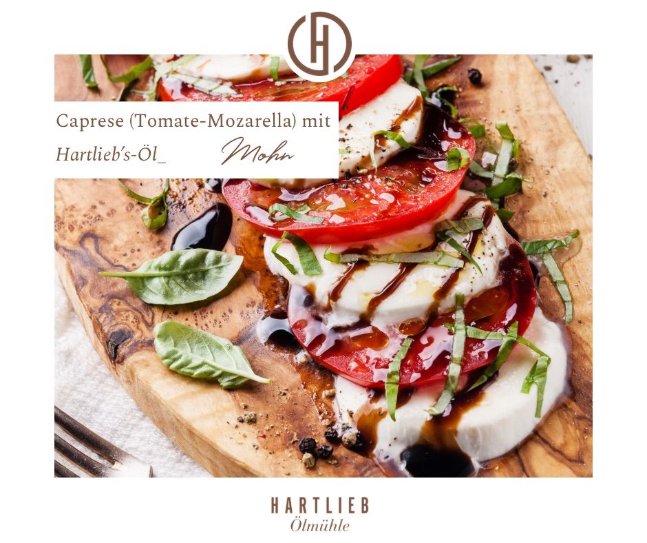 Ein Holzschneidebrett zeigt einen Caprese-Salat mit Tomatenscheiben, Mozzarella, Basilikumblättern und Balsamico-Glasur. Das Gericht ist mit Öl beträufelt und mit Pfeffer garniert. Das Bild hat einen Wasserzeichen mit dem Text Hartlieb's Öl und Mohn.