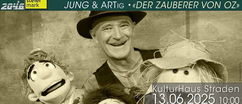 Ein alter Mann in Hut und Weste lächelt und hält Puppen bei sich, eine trägt einen Strohhut, für eine Veranstaltung von Gernot Kras.