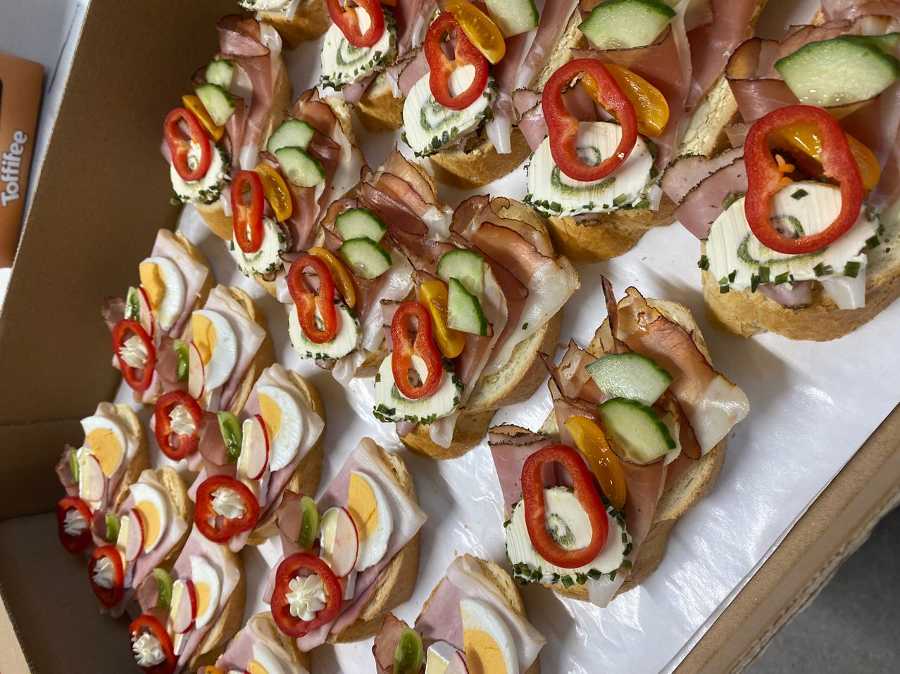 Eine Reihe von Sandwiches, jedes belegt mit Scheiben roter Paprika, Gurken und einer cremigen Aufstrich, garniert mit Scheiben Ei und Schinken.