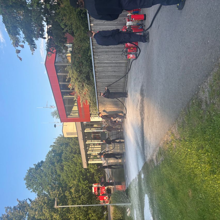 Feuerwehrleute üben mit Feuerlöschern vor einem Gebäude bei blauem Himmel.
