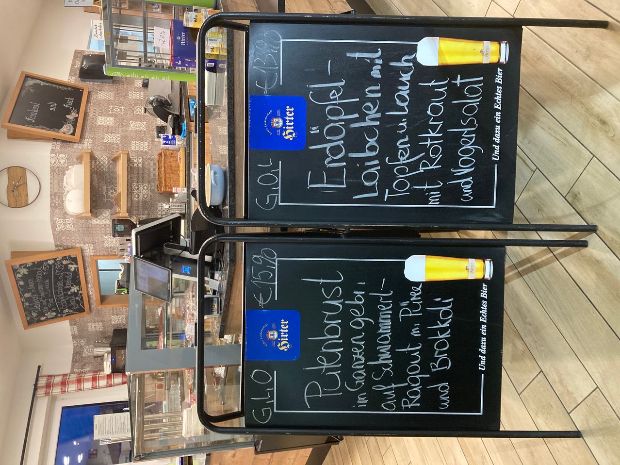 Two blackboards display beer menus with prices and descriptions. Both boards show beer names, prices in euros, and a drawing of a beer glass. The left board lists 'Erdöpfel Lauche' and 'Töpferl Lauche', while the right board lists 'Pürkbruscht' and 'Pürkbruscht Gartengetränkel'.