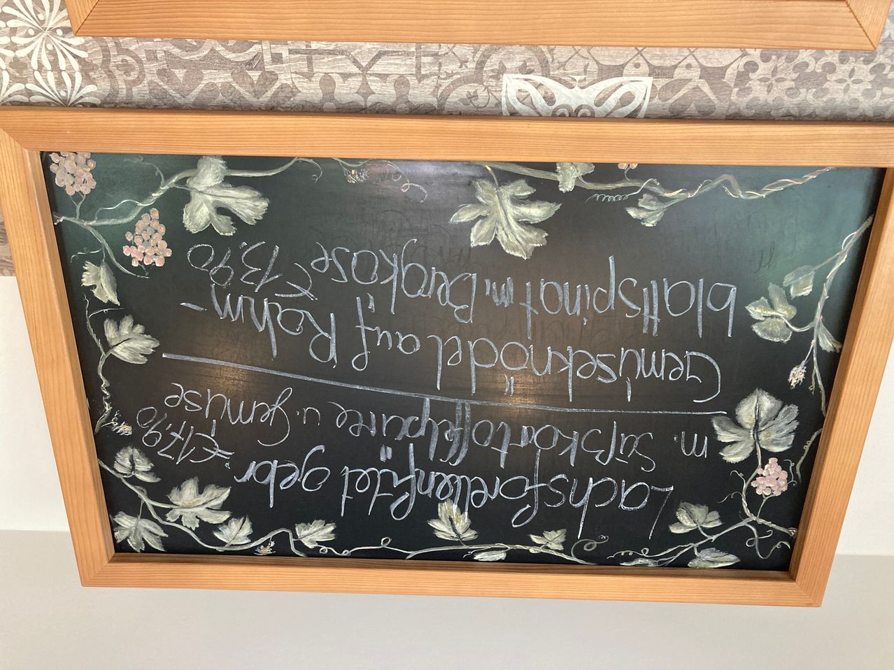 Eine Kreidetafel mit einer Nachricht, die in weißer Kreide geschrieben ist. Der Text lautet: 'Dankbarkeit verwandelt gewöhnliche Tage in Morgen mit Magie und Sinn.' Um den Text herum sind Traubenblätter und Blumen.