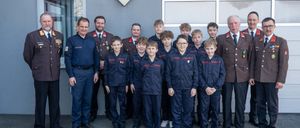 Eine Gruppe uniformierter Personen, einschließlich Erwachsener und Kinder, steht vor einem Gebäude. Sie tragen marineblaue Uniformen mit rotem Rand. Einige Erwachsene tragen Medaillen.