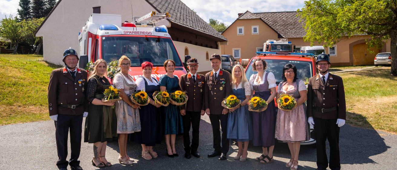 Eine Gruppe von Menschen in Uniformen und mit Sonnenblumen steht vor einem Krankenwagen und einem Feuerwehrauto.