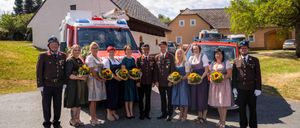 Eine Gruppe von Menschen in Uniformen und mit Sonnenblumen steht vor einem Krankenwagen und einem Feuerwehrauto.