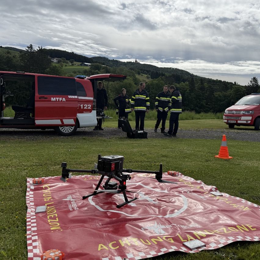 Several firefighters are standing around a red drone on a red tarp, near a red van with MTF 122 written on it.