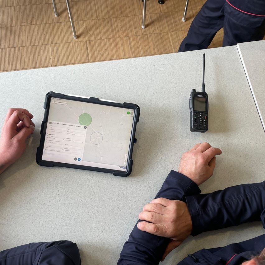 Two people sit at a table with a tablet and a radio on it. One person holds the other's hand.