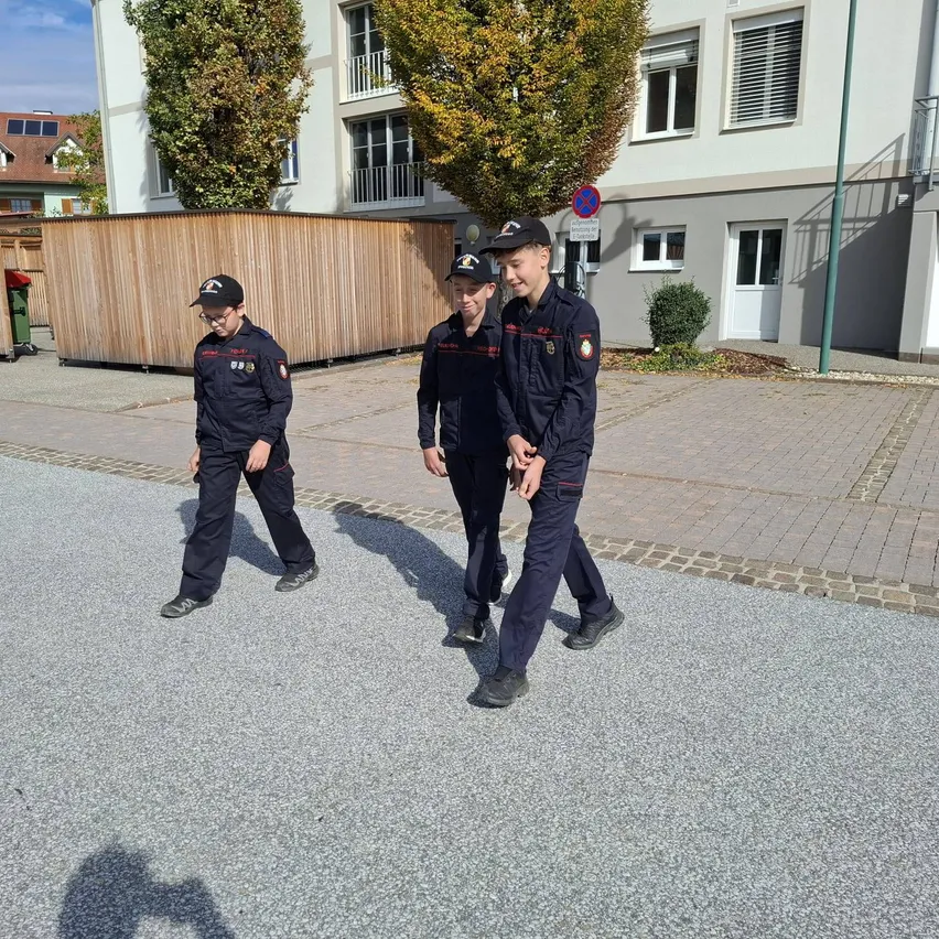 Vier junge Männer in Uniform gehen auf einem gepflasterten Straßenabschnitt vor einem Gebäude entlang.