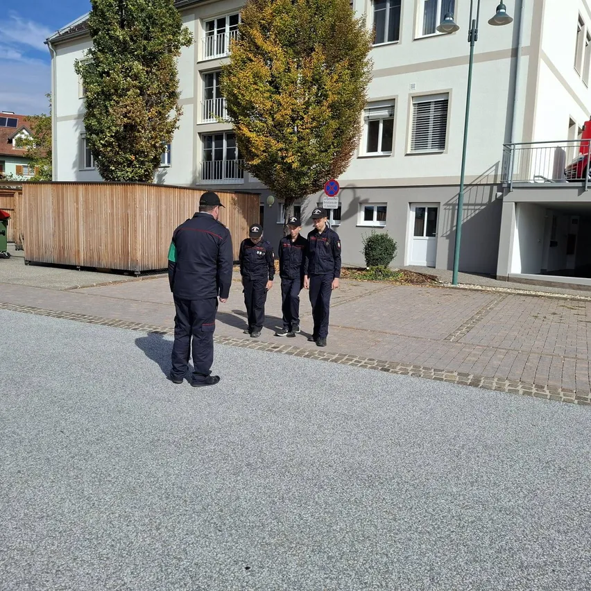 Fünf Personen gehen auf einem gepflasterten Straßenabschnitt vor einem Gebäude.