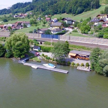 Eine Luftaufnahme eines Dorfes in der Nähe eines Flusses mit einem Steg, einem Boot, einem Haus und einer Bahnstrecke.
