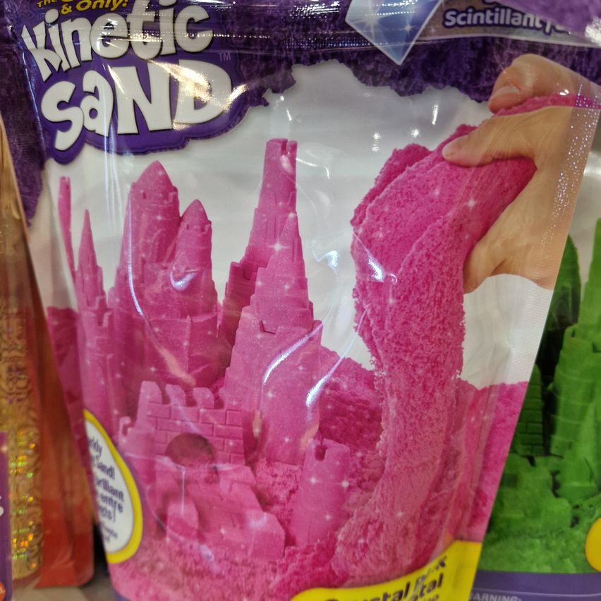 A plastic bag of pink kinetic sand, designed to sparkle and feel smooth. The bag has a squeezable section and shows an illustration of a castle.