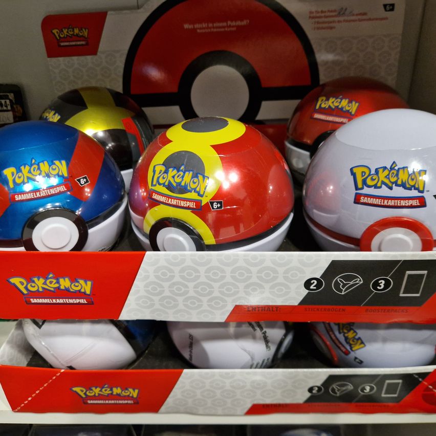 Eine Sammlung von Pokemon-Sammelkarten und Booster-Packungen ist auf einem Regal ausgestellt. Die Karten und Packungen sind in verschiedenen Farben und Größen, einige mit verschiedenen Pokemon-Charakteren.