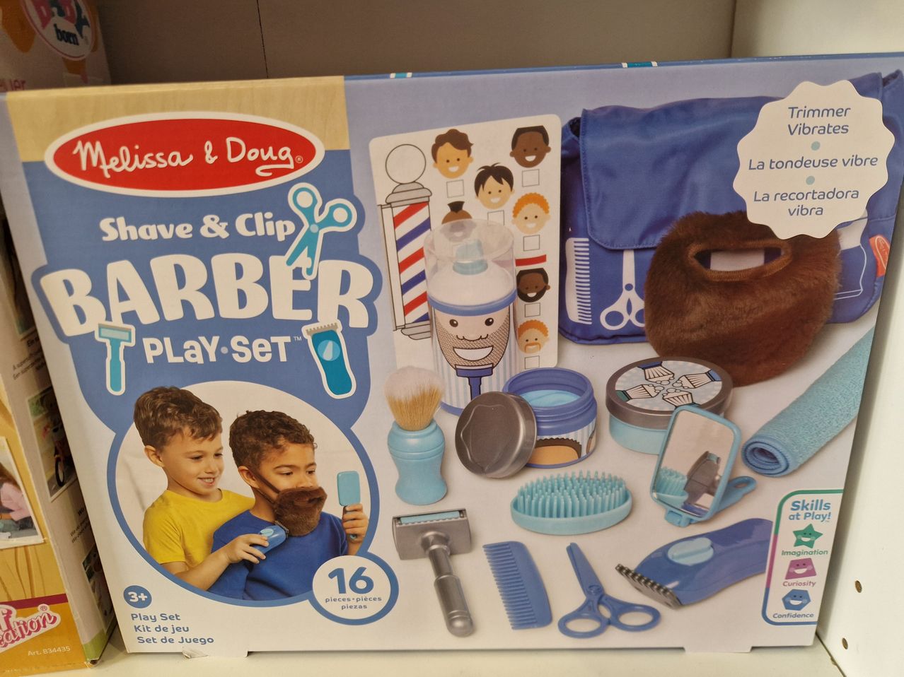 Melissa & Doug Friseur-Spielset enthält eine blaue Tasche, mehrere Pflegewerkzeuge und einen Spiegel. Es zeigt zwei Kinder, von denen eines einen Spielzeugrasierer hält. Das Paket ist für Kinder ab 3 Jahren geeignet.