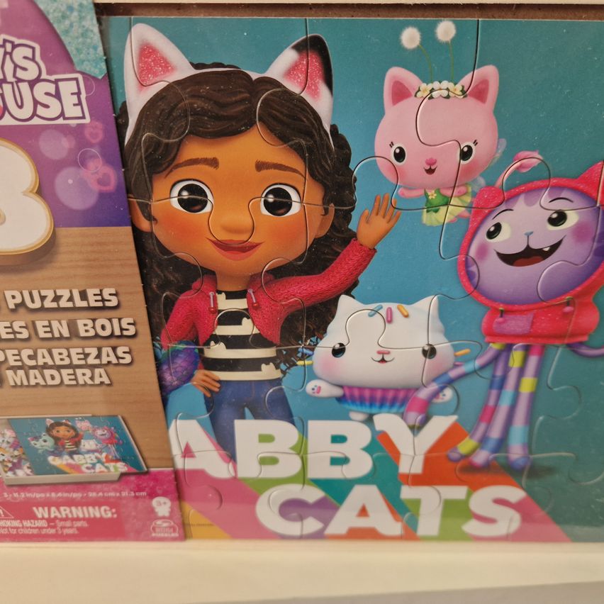 Ein Puzzle mit einer animierten Mädchenfigur mit Katzenohren, zusammen mit drei Katzencharakteren in verschiedenen Posen und Farben. Das Puzzle ist mit 'ABBY CATS' beschriftet und auf einem Holzregal platziert.