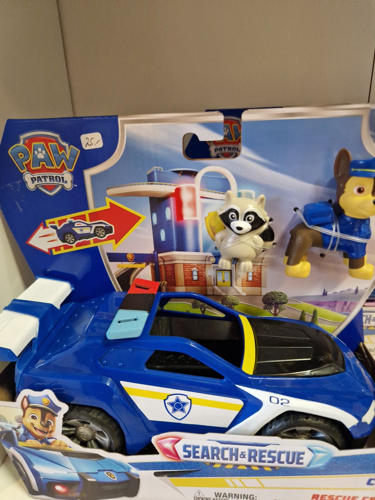 Ein blaues Spielzeug-Polizeiauto mit Paw Patrol-Thema, mit Charakteren wie einem Hund und einem Waschbären, ausgestellt auf einem Regal mit seiner Verpackung.