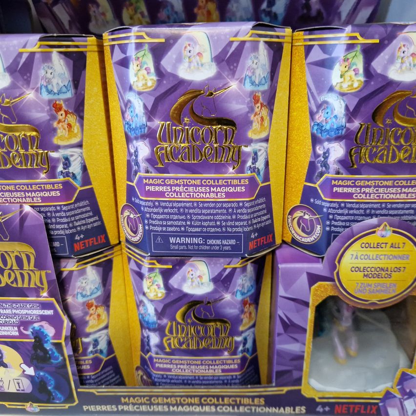 Eine Ausstellung von sammelbaren Einhorn-Figuren. Sie sind in lila und gelber Verpackung. Jede hat einen Aufkleber, der Einhornakademie lautet.