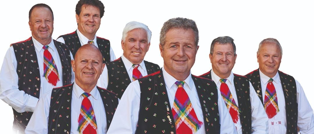Fünf Männer in traditioneller deutscher Kleidung mit roten und weißen Krawatten, lächeln für ein Foto.