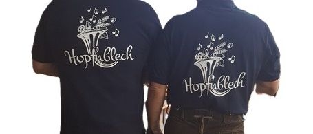 Zwei Männer in braunen Hosen und Socken, möglicherweise in traditioneller Kleidung, stehen Rücken an Rücken, jeder trägt ein dunkelblaues Shirt mit dem Schriftzug 'Hopfubrech' auf der Rückseite.