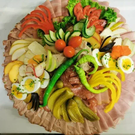 Ein großer Teller mit verschiedenen Fleischsorten, Gemüse und Früchten. Beinhaltet Scheiben von Schinken, Tomaten, Gurken, Oliven und gekochte Eier.