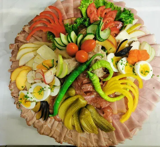 Ein großer Teller mit verschiedenen Fleischsorten, Gemüse und Früchten. Beinhaltet Scheiben von Schinken, Tomaten, Gurken, Oliven und gekochte Eier.