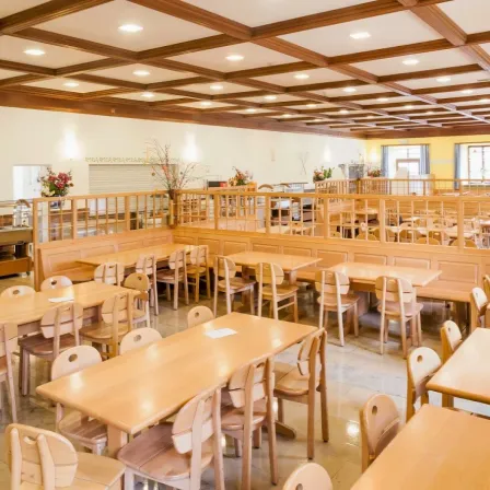 Ein Innenrestaurant mit Holztischen und -stühlen, Holzwänden und einer hölzernen Decke mit Lichtern. Es gibt Blumen in Vasen auf der Theke und Bänken.