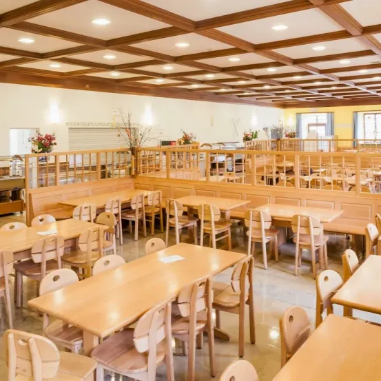 Ein Innenrestaurant mit Holztischen und -stühlen, Holzwänden und einer hölzernen Decke mit Lichtern. Es gibt Blumen in Vasen auf der Theke und Bänken.