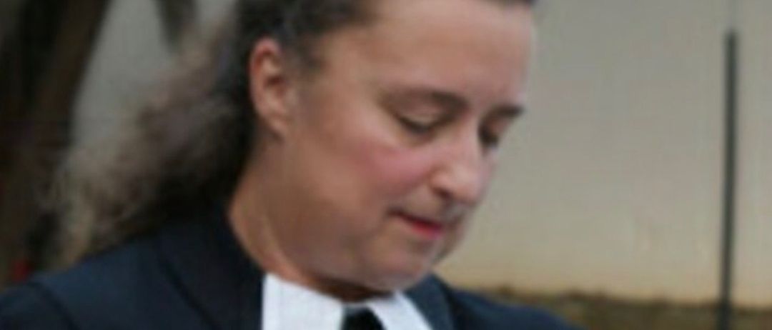 Eine Frau in einem schwarzen Gewand und einem weißen Kragen liest aus einem Buch, vielleicht in einer Kirche.
