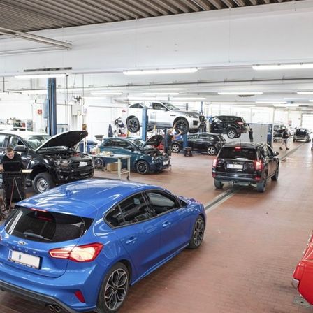 Eine Autowerkstatt mit mehreren gewarteten Fahrzeugen, darunter ein blauer Ford Focus im Vordergrund.