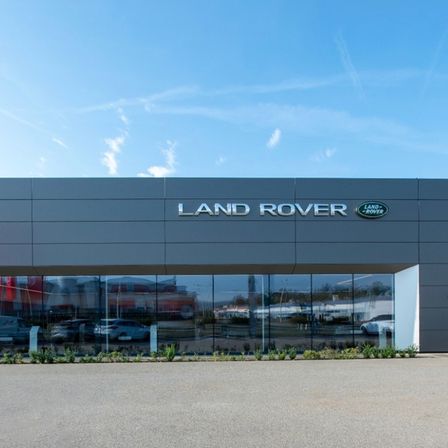 Die Vorderseite eines Land Rover-Händlers zeigt ein schlankes, modernes Design mit einem großen Logo über dem Eingang, das die Umgebung widerspiegelt.