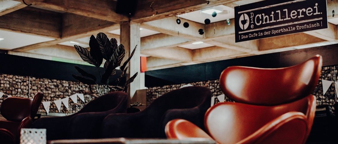 Ein Blick auf ein modernes Café mit dunklen Ledersesseln, einer großen Pflanze und einem Schild, das "Die Chie" sagt.