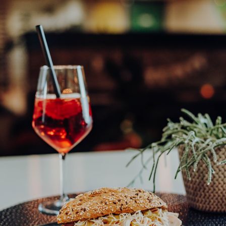 Ein Glas roter Cocktail mit Strohhalm steht neben einem Sandwich auf einem Tisch in einem Restaurant.