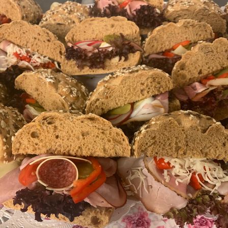 Eine Auswahl an Sandwiches mit verschiedenen Belägen wie Käse, Tomaten, Paprika und Fleisch, präsentiert auf einem Tisch mit einem Blumenhintergrund.