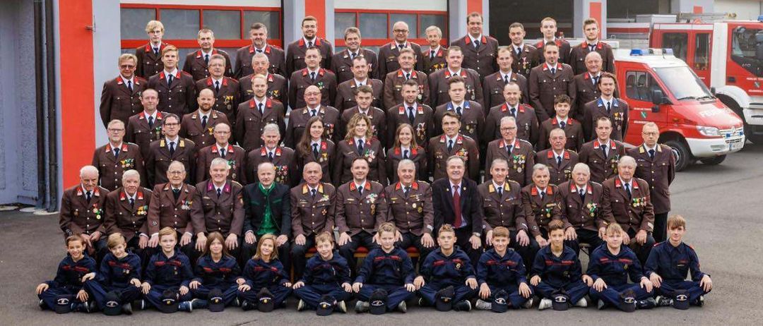 Ein Gruppenfoto der Freiwilligen Feuerwehr Heil mit mehreren Erwachsenen und Kindern in Uniform vor ihrer Feuerwache.