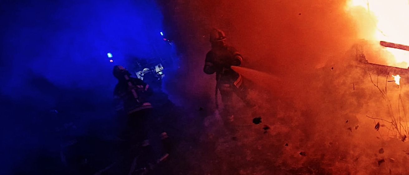 Ein Feuerwehrmann steht vor einem brennenden Fahrzeug und löscht die Flammen mit Wasser.