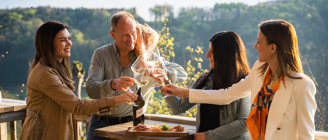 Eine Gruppe von Menschen feiert mit Weinglas in der Hand, vor ihnen steht ein Tisch mit Essen.