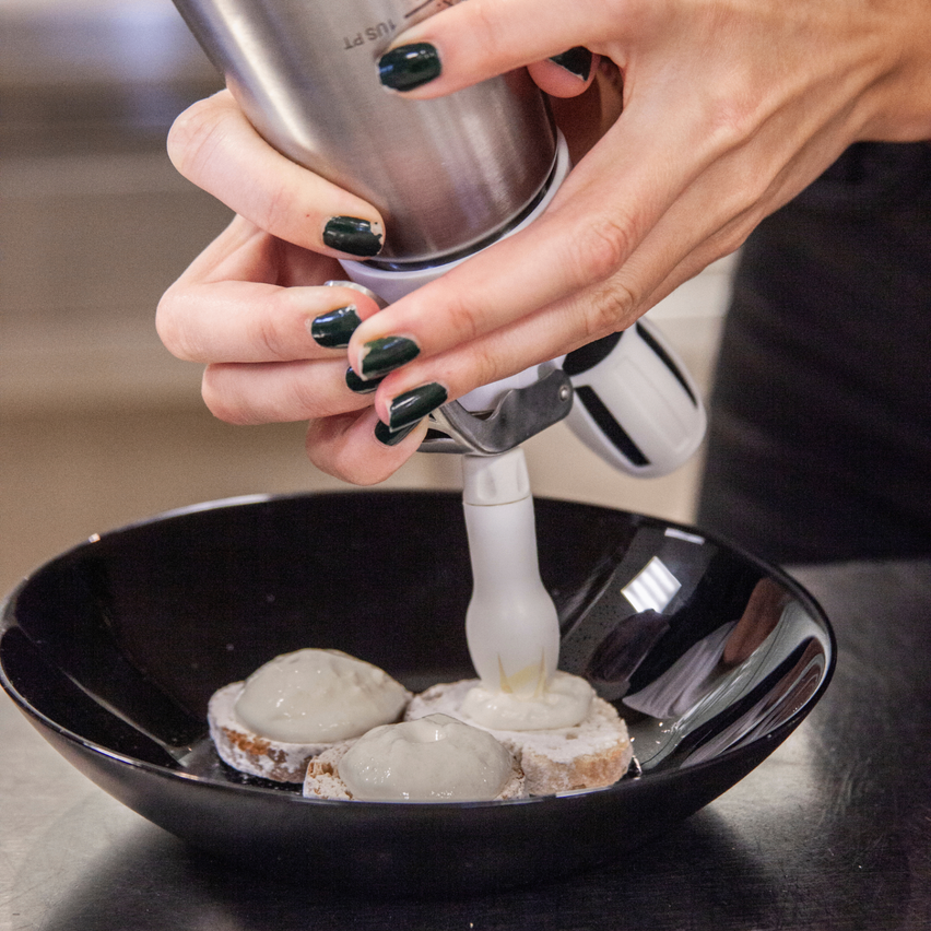 Eine Person füllt mit einer Spritztüte drei Brotscheiben mit weißer Creme in einer schwarzen Schüssel.