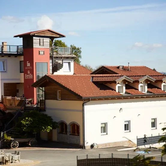 Ein Hotelgebäude mit rotem Dach und Turm. Mehrere Fenster und eine Treppe. Ein Wagen mit einem Rad davor.