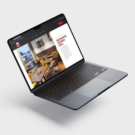 Ein Laptop zeigt eine Restaurant-Website an. Der Bildschirm zeigt ein Restaurant mit Tischen, Stühlen und einem Logo. Die Tastatur ist geöffnet, und der Trackpad ist sichtbar. Der Laptop steht auf einer weißen Oberfläche.