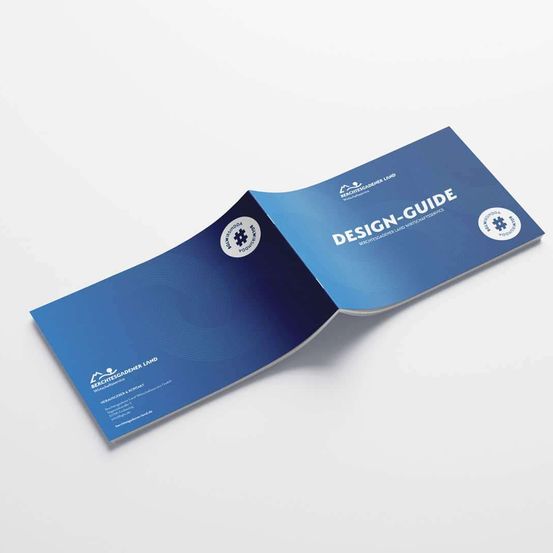 Eine blaue Broschüre mit dem Titel 'Design-Guide' ist geöffnet und zeigt beide Seiten. Sie enthält ein Logo, eine Checkliste und Text in Weiß auf blauem Hintergrund. Die Broschüre ist zur Hälfte gefaltet und zeigt die Vorder- und Innenseite.