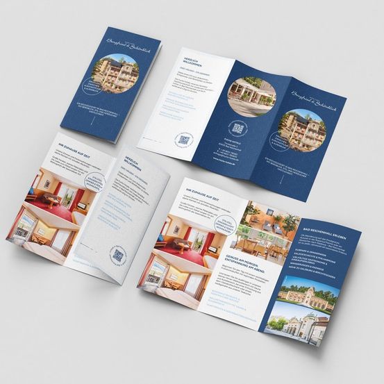 Mehrere Broschüren sind auf einer weißen Oberfläche ausgelegt. Die Broschüren zeigen Bilder eines Hotels mit blauer Decke und bieten Informationen über ein Hotel mit Zimmern, Annehmlichkeiten und Dienstleistungen. Die Broschüren haben ein blau-weißes Farbschema.