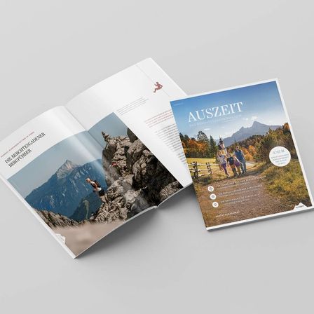 Ein offenes Magazin mit dem Titel 'AUSZEIT' und einem Foto von Menschen auf einem Pfad. Eine andere Seite zeigt einen Läufer auf einem Berggipfel.