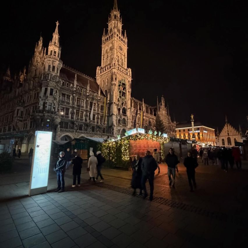 Bei Nacht gehen Menschen vor dem Neuen Rathaus in München, Deutschland, mit vielen dekorativen Lichtern herum.