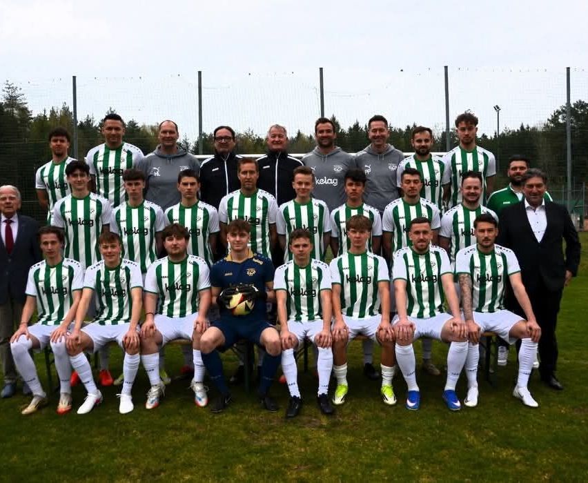 A soccer team poses for a team photo in green and white striped jerseys, with one person holding a soccer ball.