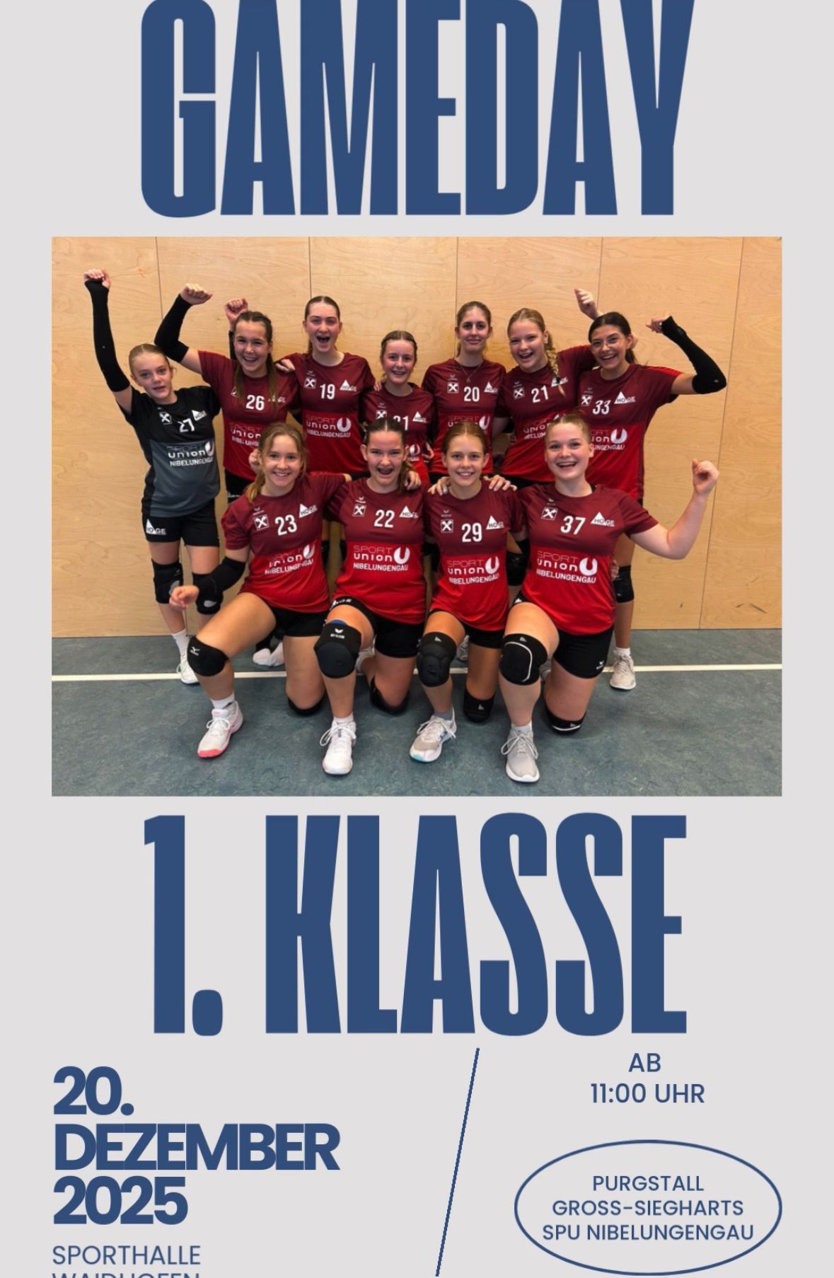 Eine Gruppe junger Athletinnen in roten Trikots posiert für ein Foto in einer Sporthalle und feiert mit erhobenen Händen. Sie tragen Knieschützer und Turnschuhe. Das Wort '1. KLASSE' steht in Blau über ihnen.