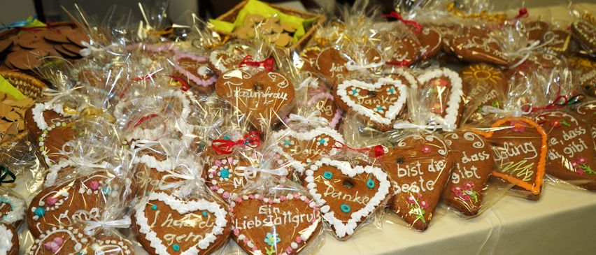 Ein Tisch voller herzförmiger Lebkuchen, einzeln in Plastik verpackt mit dekorativen Botschaften wie 'Danke' und 'Du bist die Beste'.